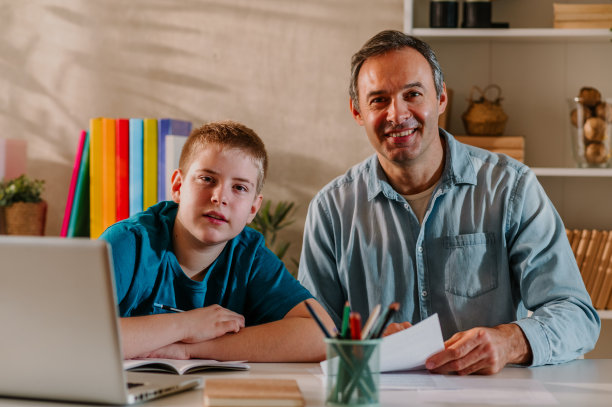 一个面带微笑的父亲和他金发碧眼的十几岁儿子看着镜头的照片。图片下载