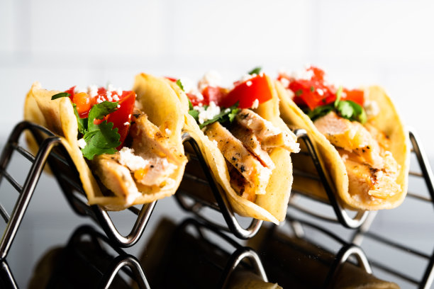 这张照片展示了三个美味的街头玉米饼，放在一个金属玉米饼架上。墨西哥卷饼色彩缤纷，配上美味的肉、新鲜的蔬菜和美味的酱汁，令人垂涎欲滴。图片下载