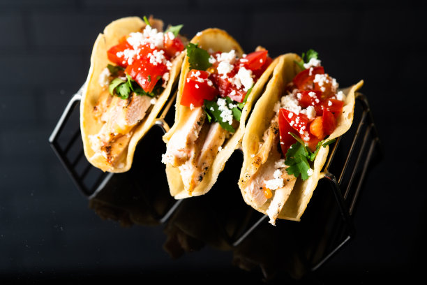 这张照片的特点是三个令人垂涎的街头玉米饼排列在一个金属玉米饼架上。鲜亮的馅料，加上上面的香菜和酸橙，构成了一顿开胃的正宗墨西哥餐。图片下载