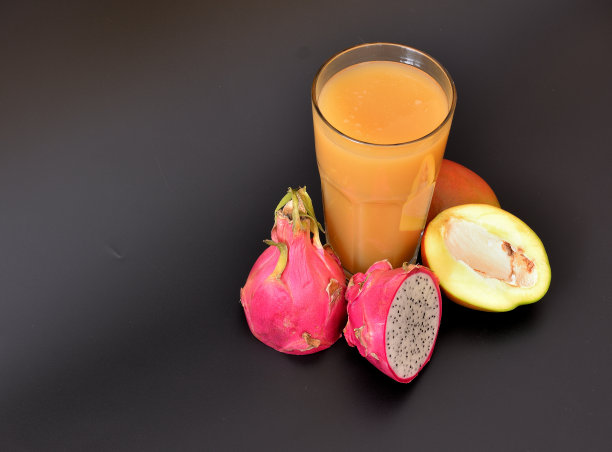 清新的果汁在黑色的背景下，旁边是半熟芒果和火龙果。图片下载