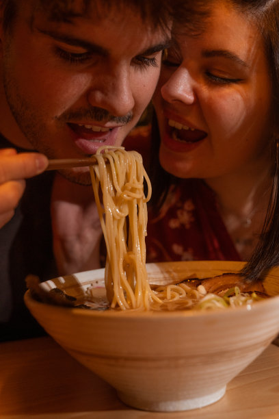 这对年轻浪漫的情侣在一起吃拉面晚餐，男孩用筷子夹着碗里的面条和他的女朋友分享。图片下载
