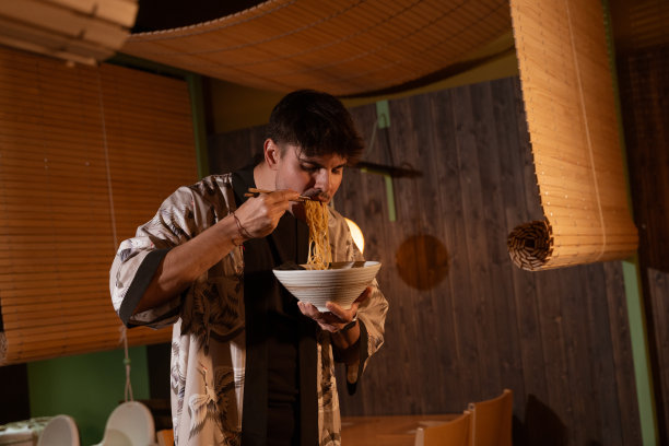 身穿日本图案和服的黑发男孩正在木墙装饰的日本料理馆里吃着日本面。图片下载