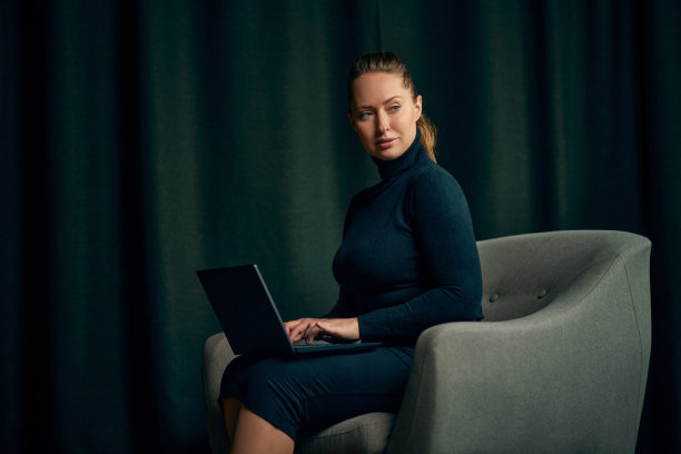 年轻优雅的商务女性坐在扶手椅上，在她的办公室里用笔记本电脑工作。自信，聪明，专业图片下载