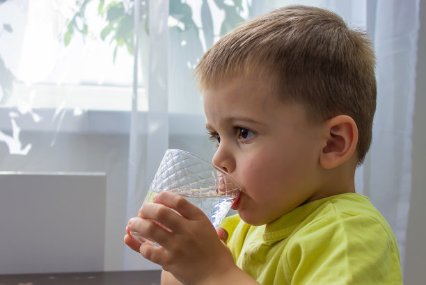 这个男孩用玻璃杯喝水。纯水。夏天。图片下载