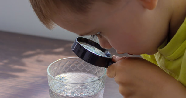 孩子用放大镜检查玻璃杯里的水。有选择性的重点。图片下载