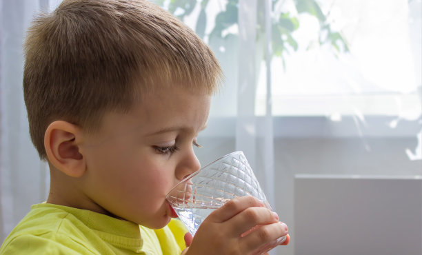 这个男孩用玻璃杯喝水。纯水。夏天。图片下载