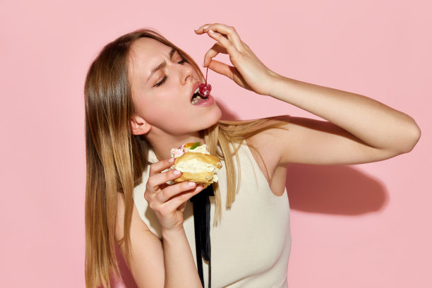 一个美丽的模特吃着蛋糕，粉红色的背景上有愉快的面部表情图片下载