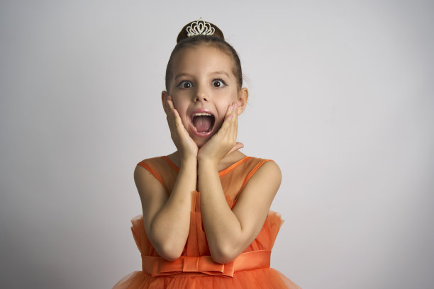 可爱的小女孩穿着橙色的裙子在白色的背景上摆姿势图片下载