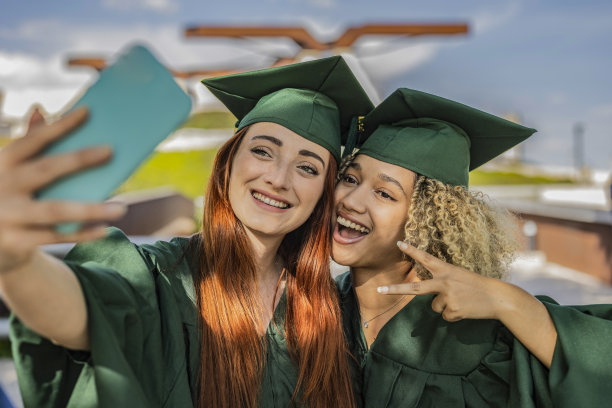 毕业日，两个刚毕业的多种族女孩一起用智能手机自拍图片下载