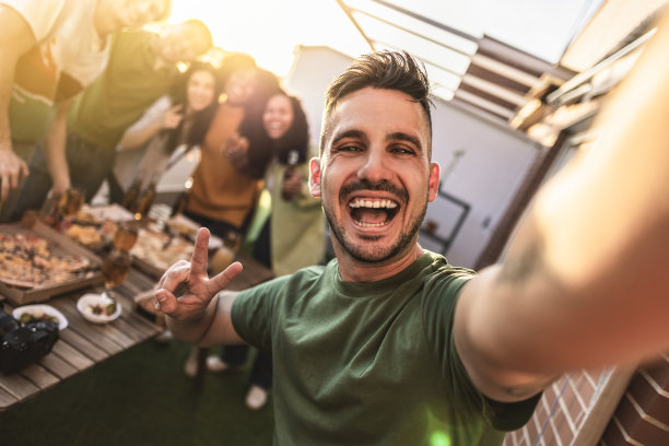 一群不同的年轻朋友在屋顶上聚会，吃，喝，自拍，专注于英俊的家伙微笑图片下载