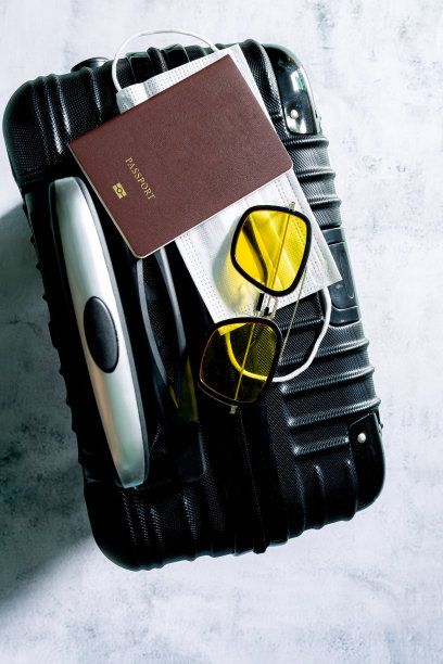 人类的手拖着行李,行李,行李箱,护照和医疗面具,手拿着护照和批准疫苗接种卡和电脑包行李准备出差。旅客的疫苗证明和公民身份证明;图片下载