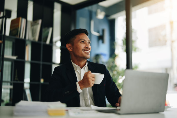 一位亚洲男性企业家在投资成功后，站在电脑前露出喜悦的表情图片下载