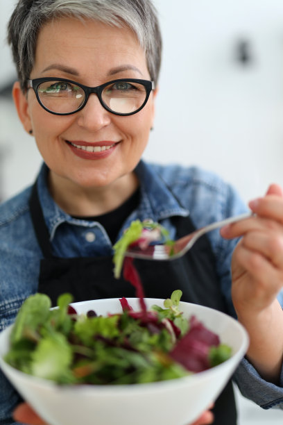 一个成熟、积极的素食女性的特写，她手里拿着一盘沙拉。图片下载