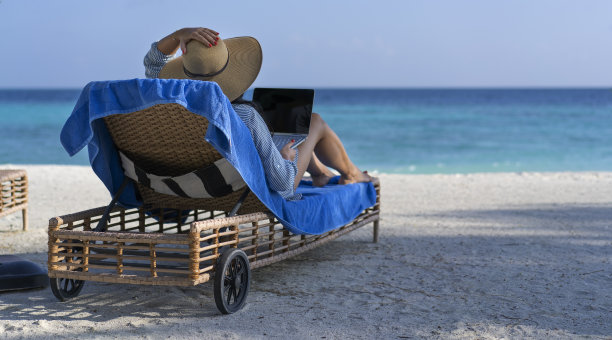 一名年轻女子在马尔代夫的海滩上用笔记本电脑工作。远程工作和游牧的概念图片下载