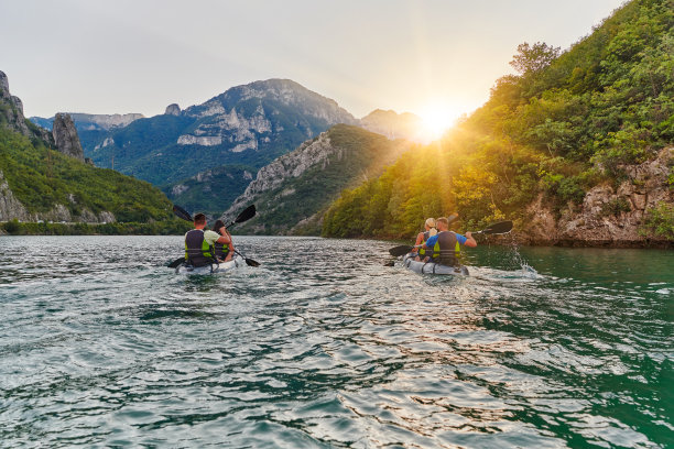 一群朋友享受乐趣和皮划艇探索平静的河流，周围的森林和大的天然河谷在田园诗般的日落。图片下载