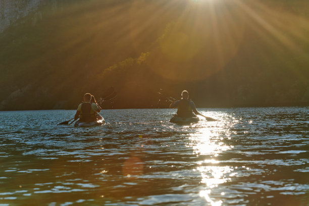 一群朋友享受乐趣和皮划艇探索平静的河流，周围的森林和大的天然河谷在田园诗般的日落。图片下载