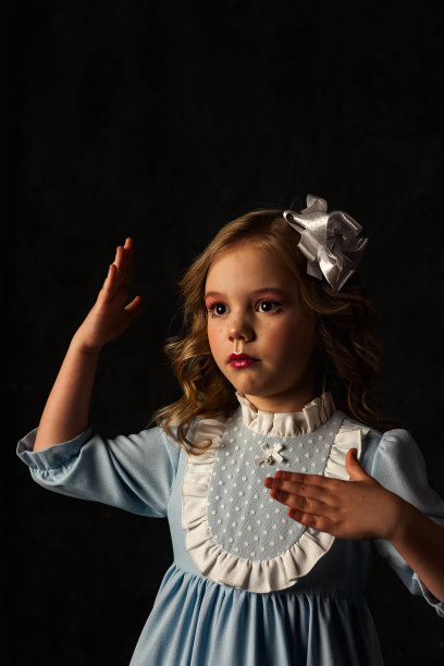 可爱的小娃娃封面女孩的手在黑色的背景，看向别处。可爱的孩子穿着蓝色的衣服，头上戴着白色的蝴蝶结，与光和影隔绝。时尚形象理念。复制广告文本空间图片下载