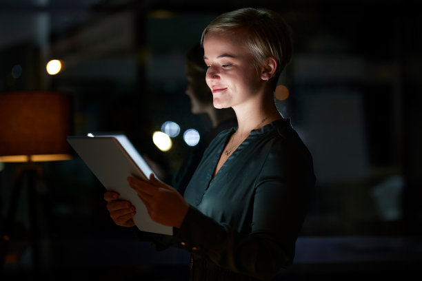 工作，加班，带着平板电脑，微笑着上网搜索，在数字设计项目上工作到很晚。漆黑的夜晚，设计师在办公室里阅读在线市场研究报告。图片下载