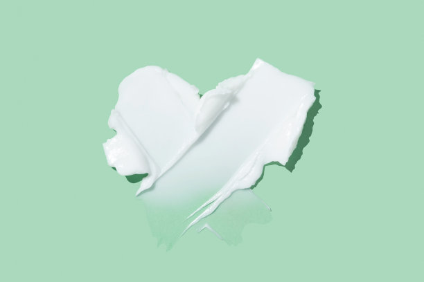 美容护肤霜质地刷样在心形。白色美容霜涂抹污迹孤立在绿色背景图片下载