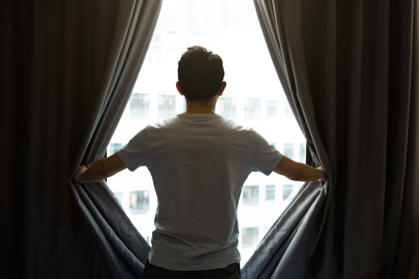 一个男人打开卧室的窗帘，寻找一种新的、充满希望的生活方式——一种健康的生活方式图片下载