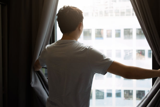 一个男人打开卧室的窗帘，寻找一种新的、充满希望的生活方式——一种健康的生活方式图片下载