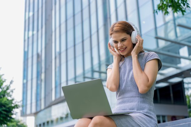漂亮的女商人带着耳机和笔记本电脑在户外听音乐和看在线视频图片下载