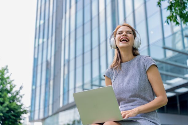 漂亮的女商人带着耳机和笔记本电脑在户外听音乐和看在线视频图片下载