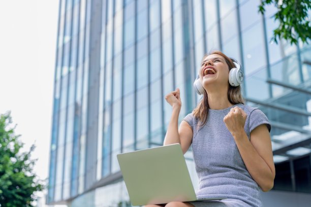 漂亮的女商人带着耳机和笔记本电脑在户外听音乐和看在线视频图片下载