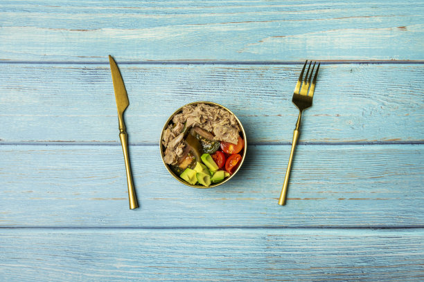 蓝色的桌子上放着一幅静物画和沙拉，上面有各种各样的西红柿丁、鳄梨丁和很多金枪鱼罐头，用金色的餐具图片下载