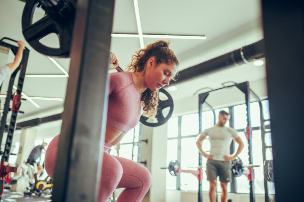 一个强壮的女健美运动员在健身房里蹲着举杠铃的低角度照片。图片下载