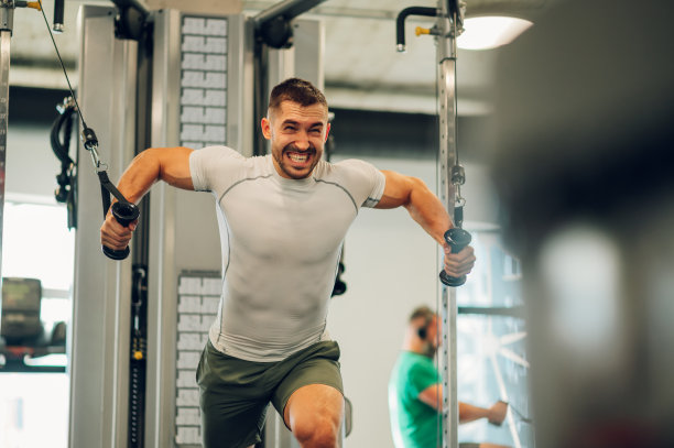 健身房里，一个肌肉发达的男子正皱着眉头在拉绳机上举重。图片下载
