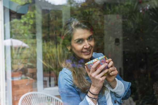 一位拉丁裔妇女站在她的情感治疗师办公室的窗前，享受着一杯咖啡图片下载