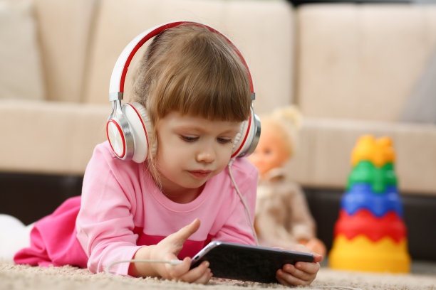 戴着耳机的小女孩躺在地板上拿着智能手机图片下载