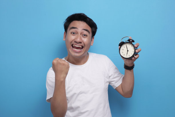 年轻的亚洲学生拿着闹钟庆祝胜利图片下载