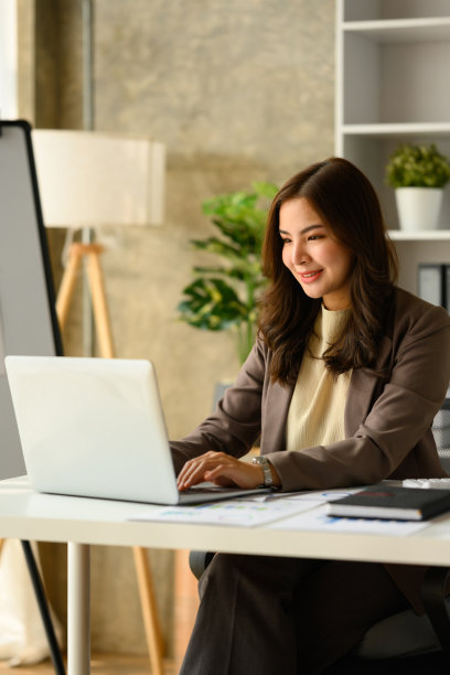 女性创业者坐在现代办公室里，用笔记本电脑工作的照片。图片下载