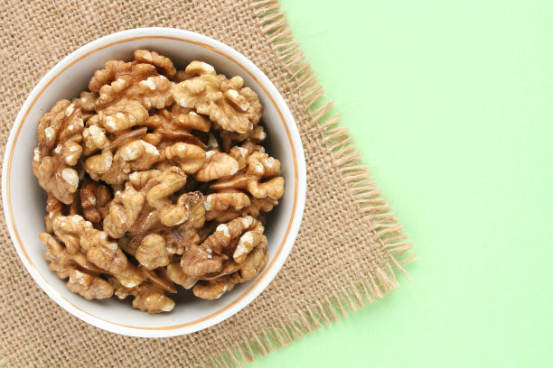 白色陶瓷碗上的胡桃木和绿色背景上的生态帆布餐巾。健康饮食，营养饮食，素食理念图片下载