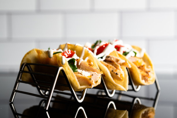 这张令人垂涎的照片展示了三个美味的街头玉米饼在一个金属玉米饼架上。墨西哥卷饼里塞满了美味的肉、五颜六色的配料和新鲜的香草，使它们成为眼睛和胃的盛宴。图片下载