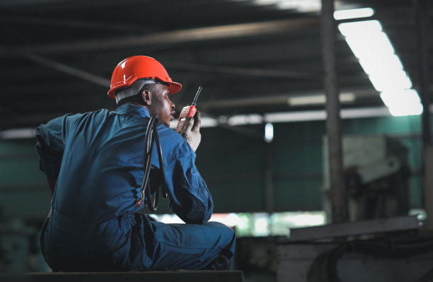 在重工业制造工厂，穿着防护服的工程师或工人坐在那里使用对讲机对讲机，同时戴着安全帽和电缆线控制工作图片下载