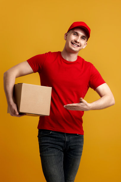 头戴红帽、身穿t恤的快递员手里拿着纸板箱图片下载