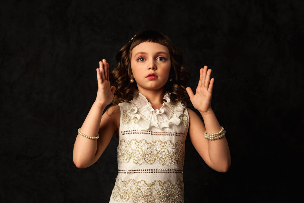 封面小娃娃女孩的肖像，穿着白色的衣服，在黑色的背景上手势，向前看。可爱的孩子7-8岁孤立在阴影、黑暗中。剧场表演概念。复制文本空间图片下载