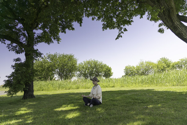 一个女人在公园的树荫下做冥想瑜伽图片下载