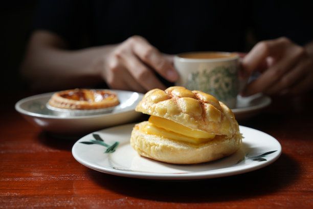 图为一名年轻的亚洲女子在当地一家茶餐厅享用新鲜出炉的港式马球包和蛋挞，外加一杯牛奶咖啡。图片下载