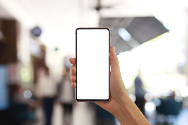 一只手拿着空白屏幕的智能手机，背景是一个购物中心的模糊背景。图片下载