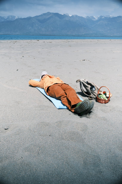 一位女背包客正躺在山湖沙滩上的垫子上图片下载