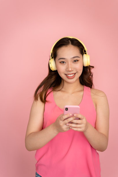 微笑的女人手里拿着一部粉红色的智能手机，背景是相配的。图片下载