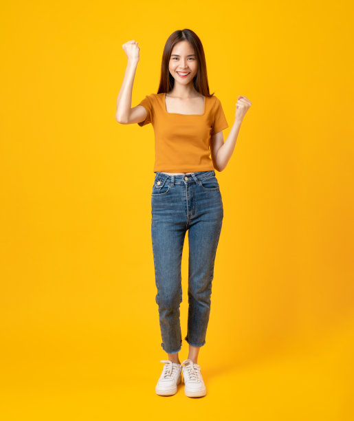 快乐微笑的年轻女子穿着休闲的橙色t恤，展示举起拳头，孤立在黄色背景上。图片下载