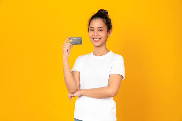 开朗美丽的亚洲女人拿着黄色背景的信用卡模型。图片下载