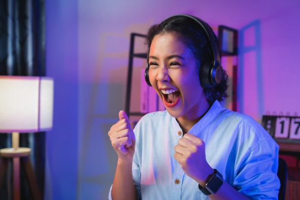 年轻的亚洲女子戴着耳机，双手举起双臂，握紧拳头，显示出强大的力量，庆祝胜利，表达成功。图片下载