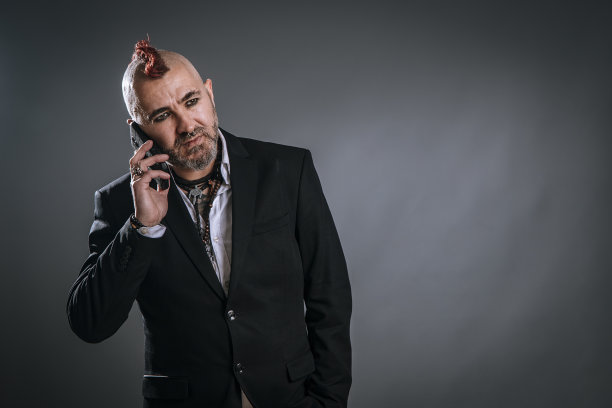 商人出席手机与朋克风格在工作室拍摄灰色背景图片下载
