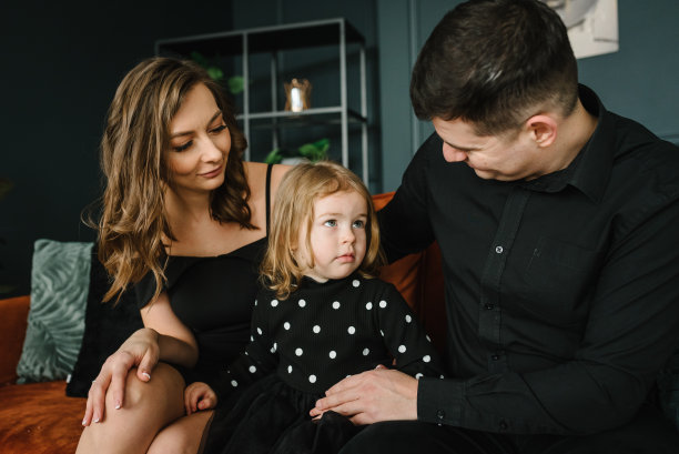 女儿拥抱并祝贺父亲，母亲特写。孩子微笑着拥抱爸爸，妈妈放松地躺在家里客厅的沙发上。家人欢笑和拥抱。愉快的一天。家庭度假的照片。图片下载